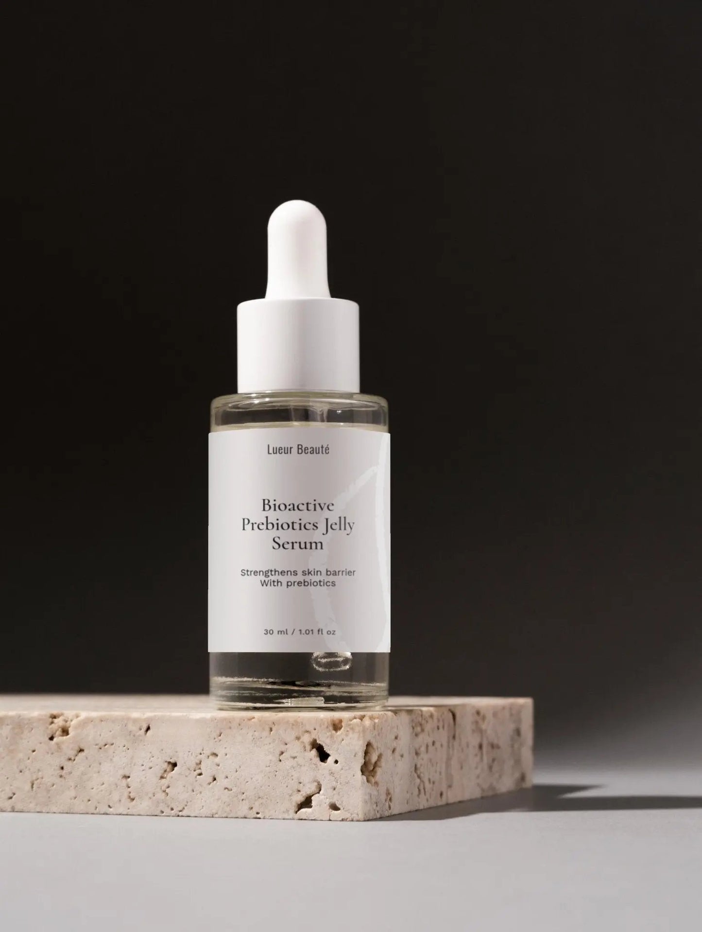 Lueur Beauté Bioactive Prebiotics Jelly Serum bottle standing on a stone podium in a minimalist studio setting with soft shadows.