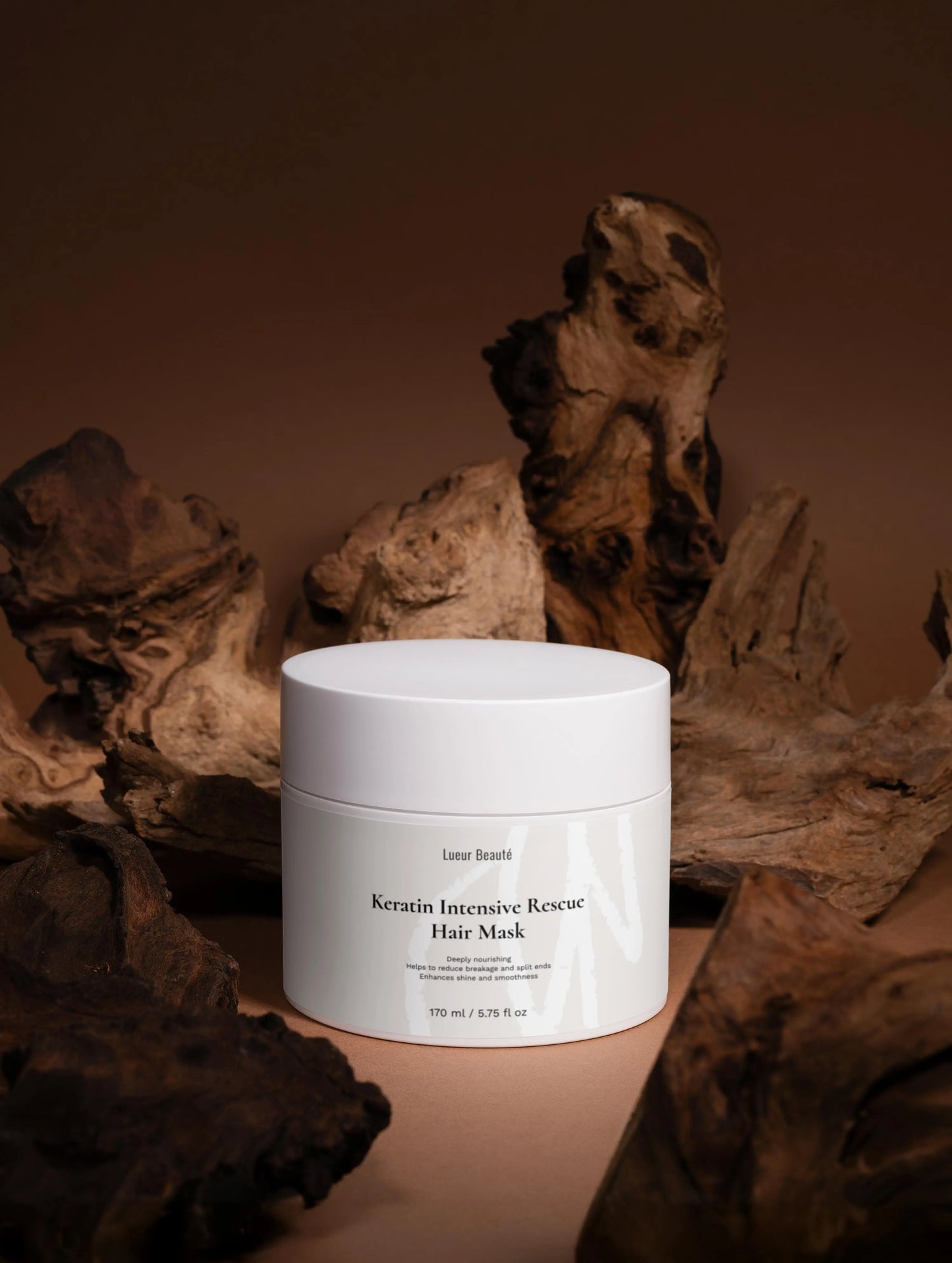 Lueur Beauté Keratin Intensive Rescue Hair Mask jar styled with natural driftwood on warm brown background