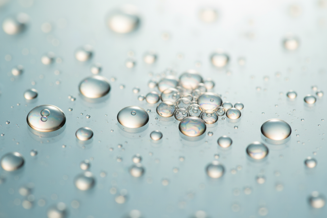 Abstract macro of translucent liquid droplets on glass — exfoliation guide AHA vs BHA vs enzymes by Lueur Beauté