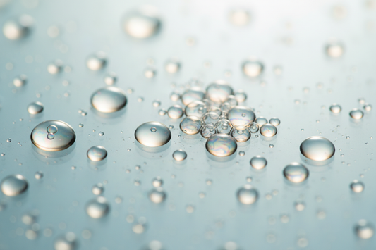 Abstract macro of translucent liquid droplets on glass — exfoliation guide AHA vs BHA vs enzymes by Lueur Beauté