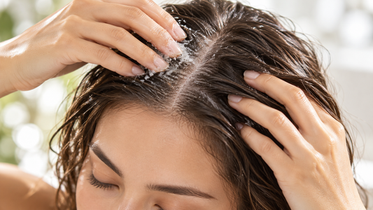 Close-up of a woman gently applying a scalp scrub to the scalp with parted hair