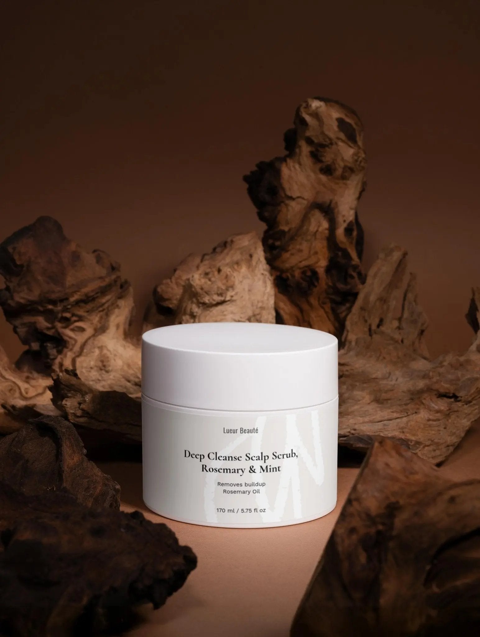 Lueur Beauté Deep Cleanse Scalp Scrub with rosemary and mint displayed in a studio setting with dark natural wood textures in the background.