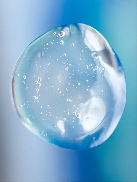 Close-up of a transparent gel droplet with small air bubbles against a blue background.