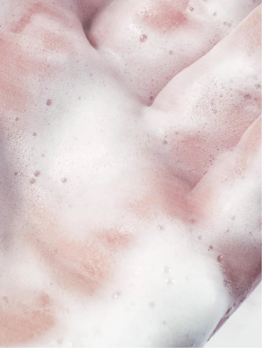 Close-up of a hand covered in white foam and small soap bubbles.