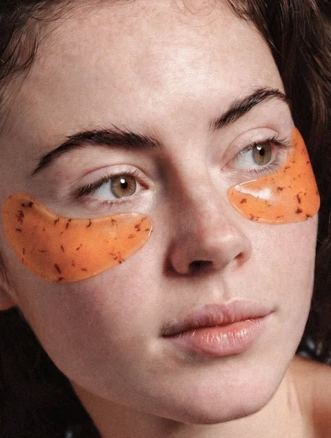 Woman wearing orange hydrogel under eye patches for tired and puffy-looking eyes