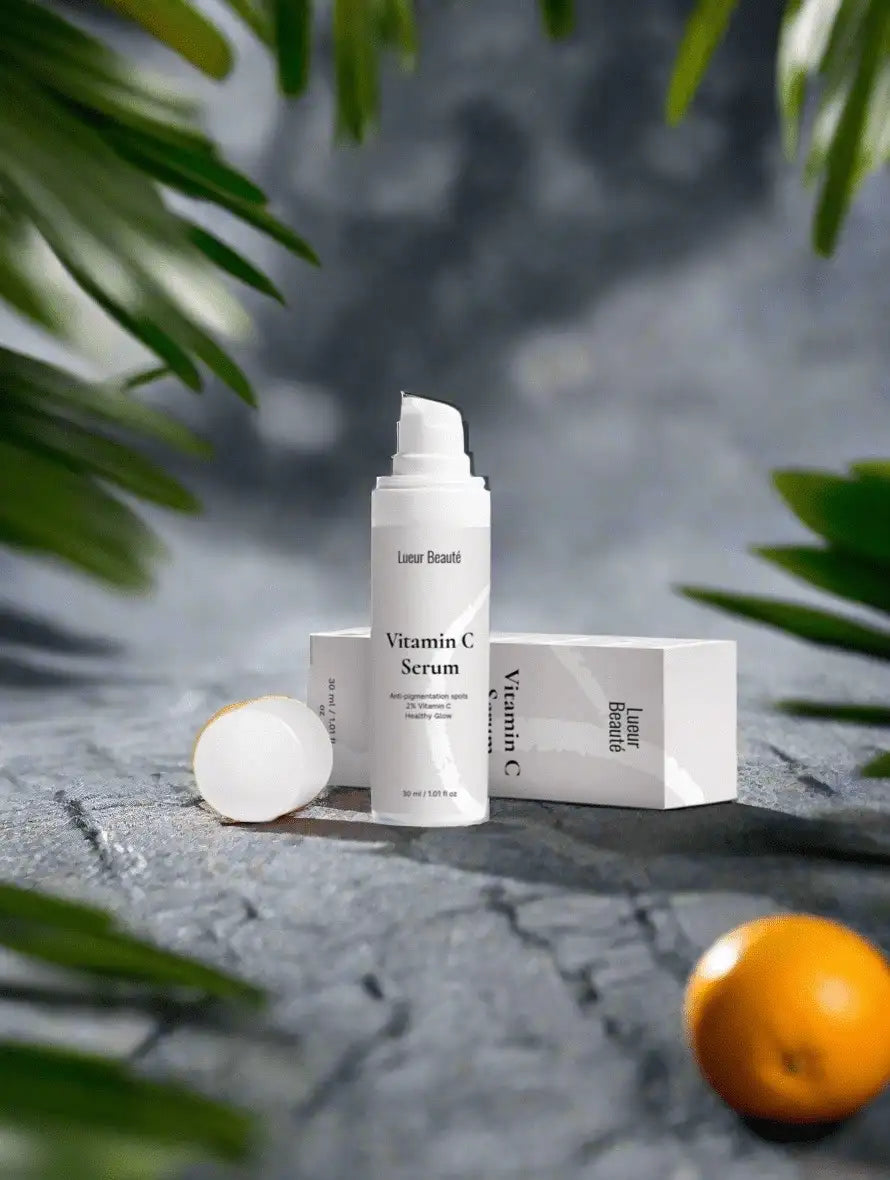 Lueur Beauté Vitamin C Serum product photo with bottle and box on a natural stone background, surrounded by green leaves and an orange.